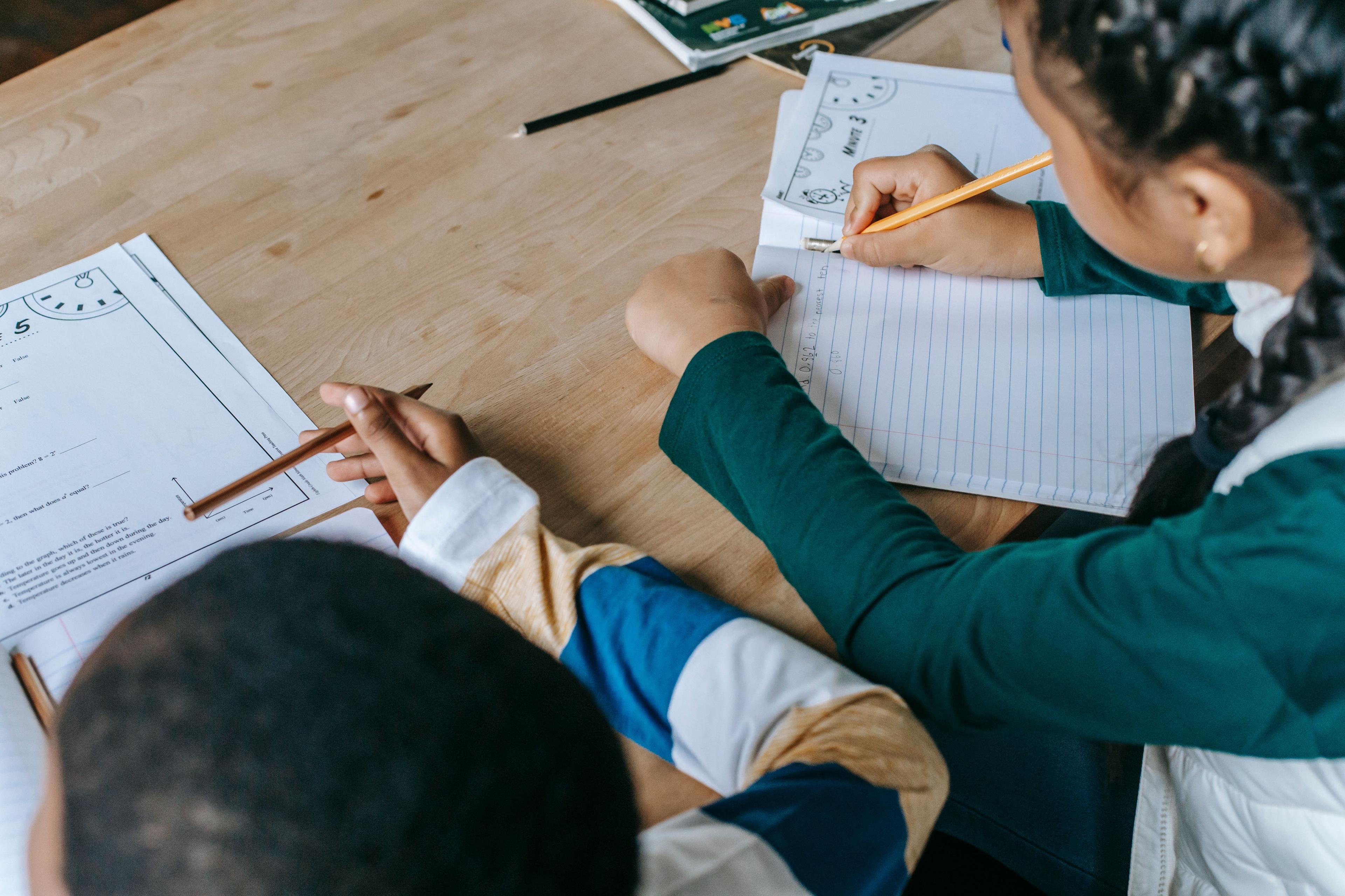 Two children studying together at a desk, writing in notebooks during a tutoring session